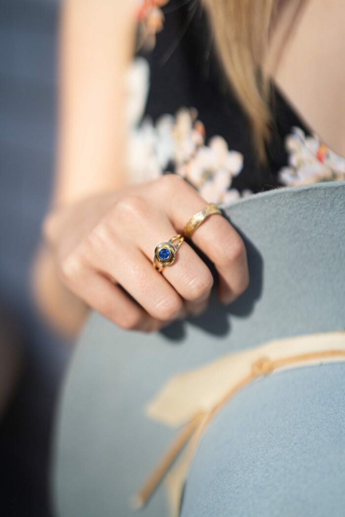 Dorothee Rosen 18k Yellow Gold ring with sapphire and 100% Fairmined Eco gold ring with hat in hand on model